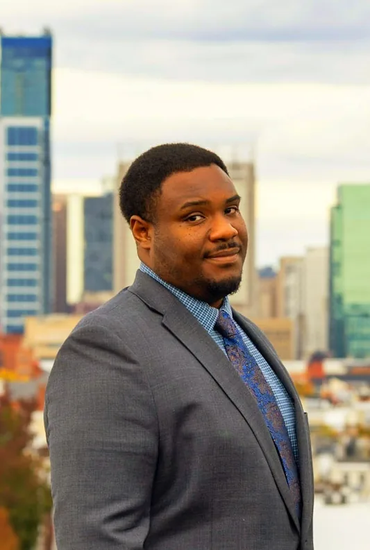 Nick Poole, web developer, standing on a rooftop with the Baltimore skyline behind him